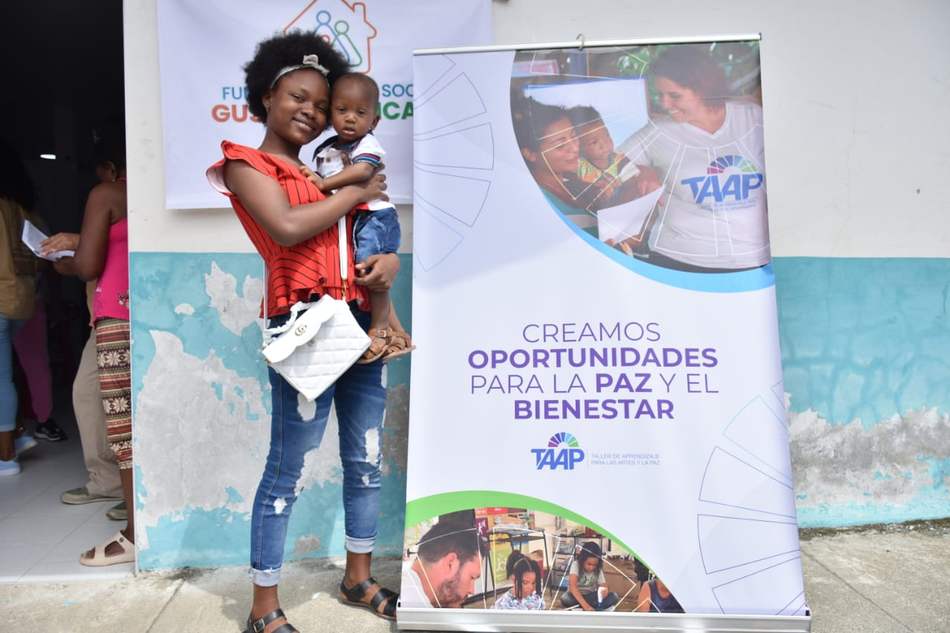 Madre joven con su hijo junto al banner de oportunidades para la paz de Fundación TAAP